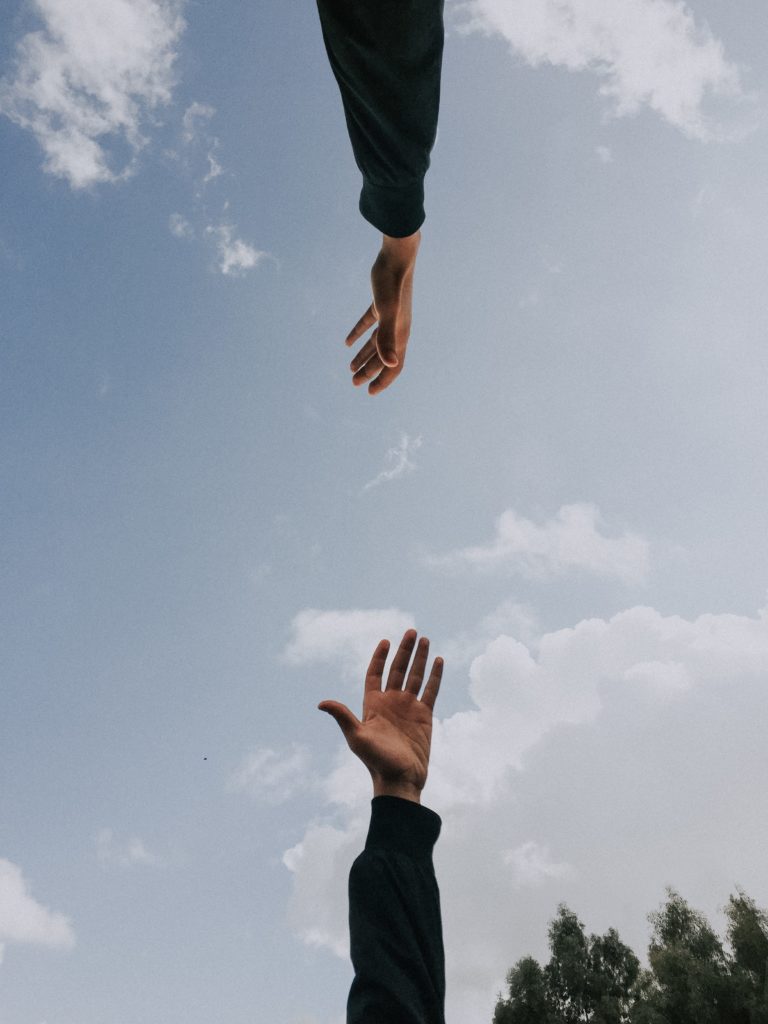 Two hands reaching for each other with blue sky in the background